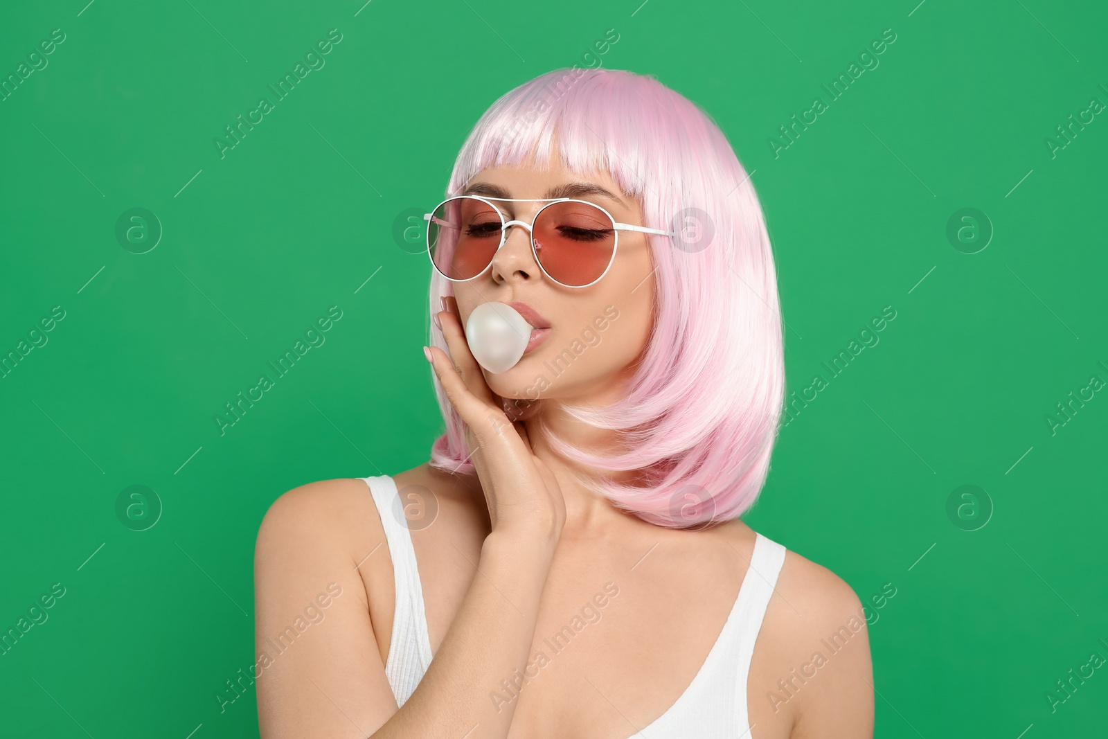 Photo of Beautiful woman in sunglasses blowing bubble gum on green background