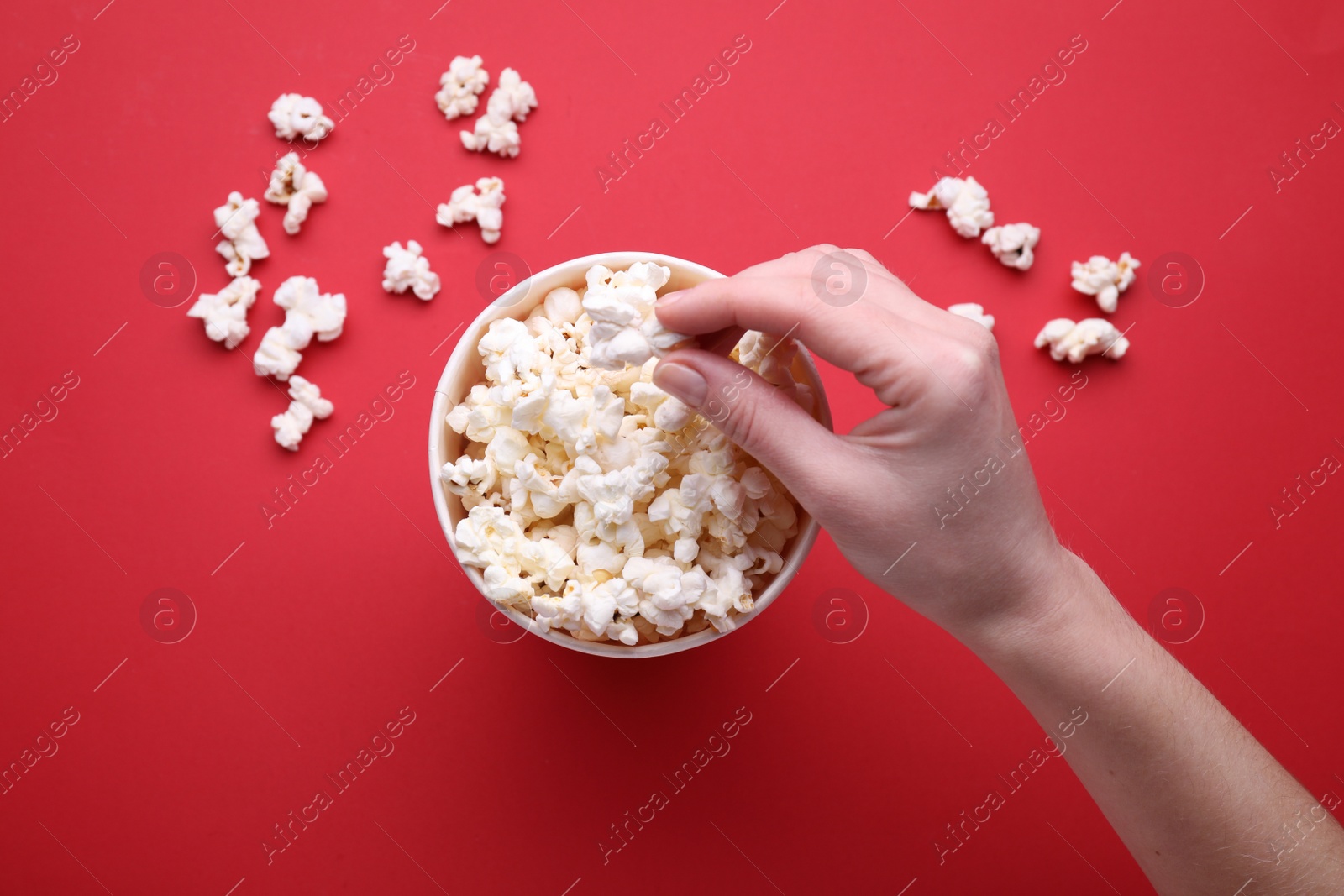 Photo of Woman taking delicious popcorn from paper bucket on red background, top view