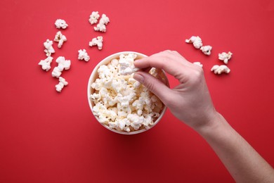 Woman taking delicious popcorn from paper bucket on red background, top view