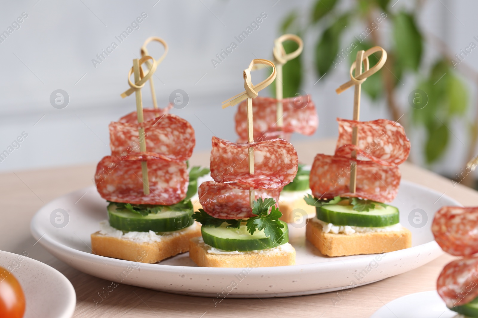 Photo of Tasty canapes with salami, cucumber and cream cheese on light table, closeup