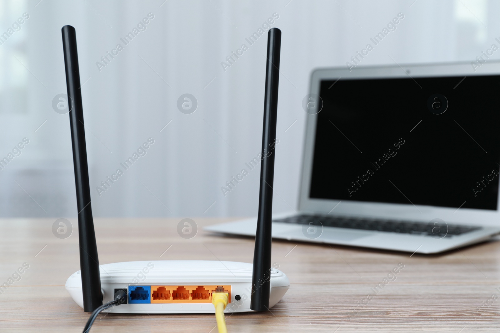 Photo of Modern Wi-Fi router and laptop on wooden table indoors