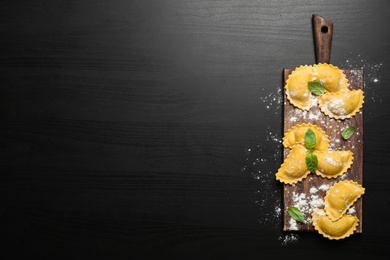 Raw ravioli with basil on black wooden table, flat lay and space for text. Italian pasta