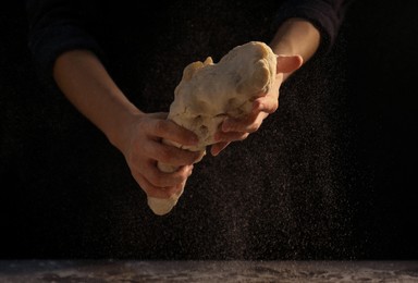 Making bread. Woman kneading dough at table on dark background, closeup