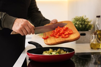 Photo of Cooking process. Man adding cut bell pepper into frying pan in kitchen, closeup