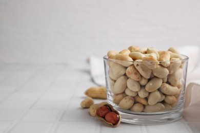 Photo of Roasted peanuts in bowl on white tiled table. Space for text