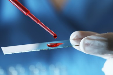 Photo of Scientist dripping sample of red liquid onto microscope slide, closeup