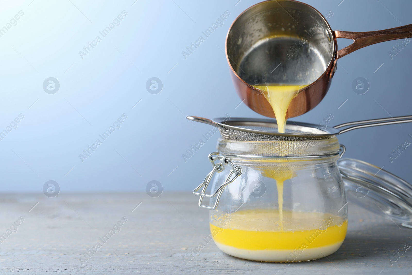 Photo of Pouring clarified butter into jar on grey table. Space for text