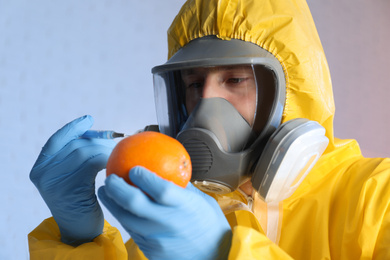 Photo of Scientist in chemical protective suit injecting orange on color background