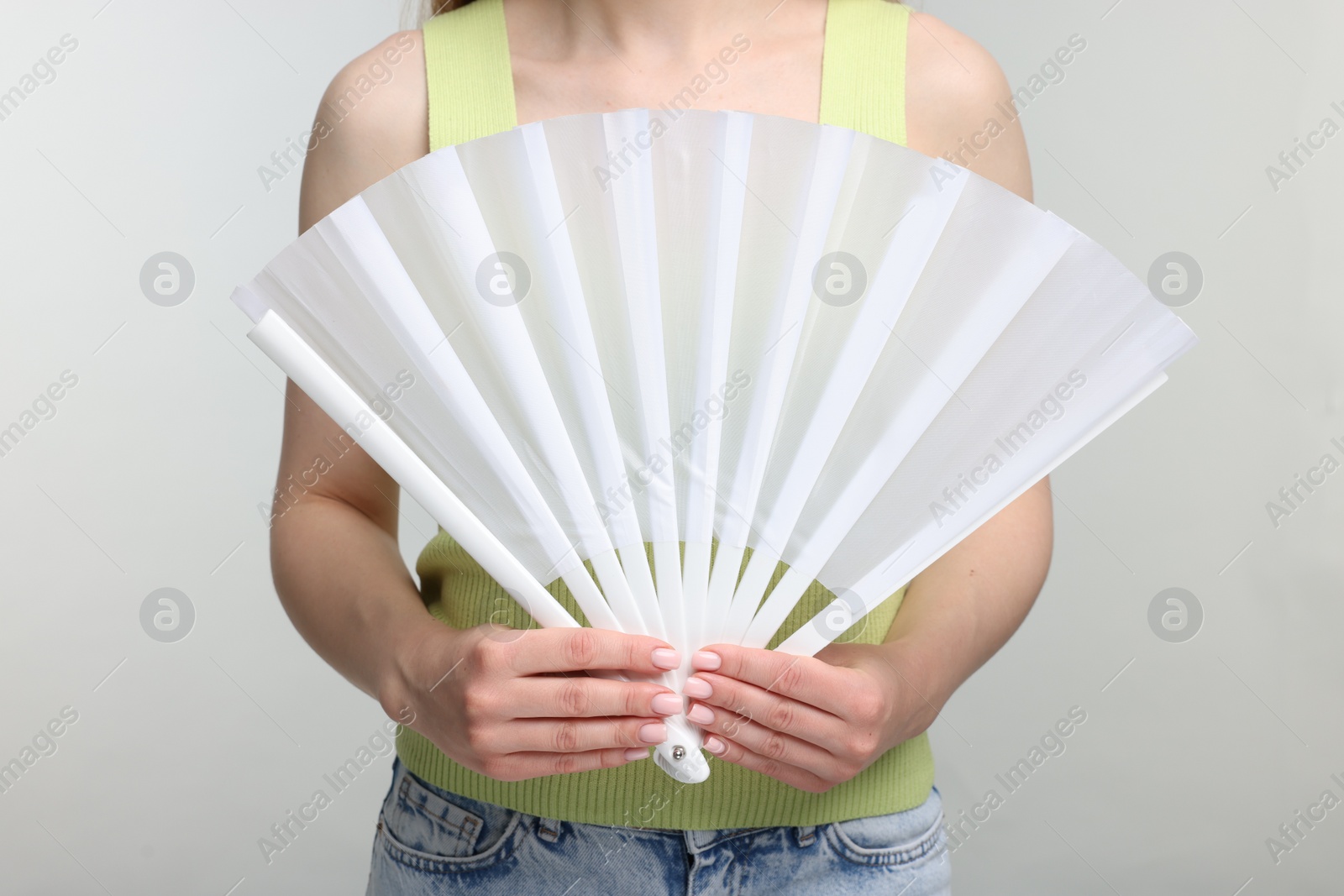 Photo of Woman with white hand fan on light grey background, closeup