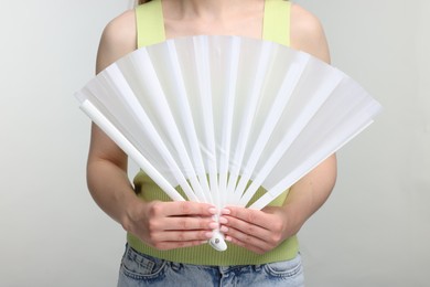 Photo of Woman with white hand fan on light grey background, closeup