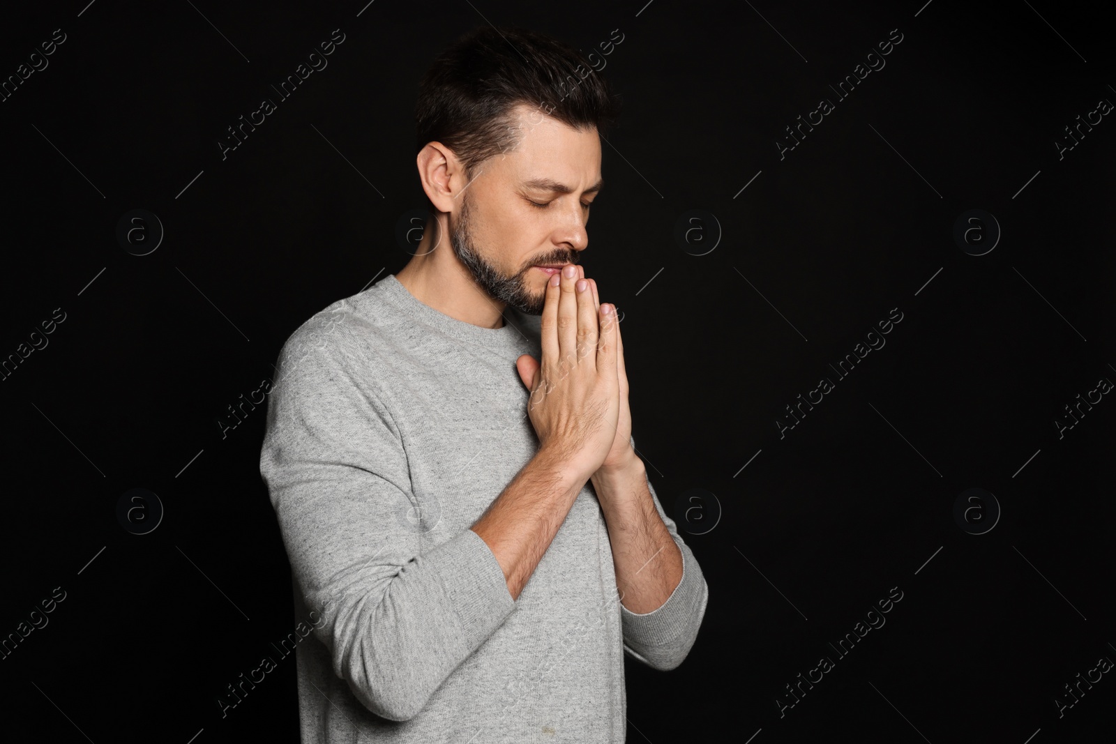 Photo of Man with clasped hands praying on black background