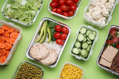 Photo of Different containers with fresh products on light green background, flat lay