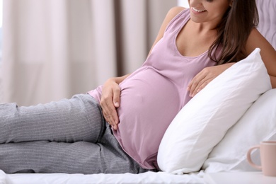 Happy pregnant woman lying on bed at home, closeup