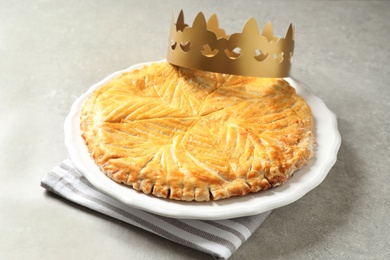 Traditional galette des Rois with paper crown on light grey table