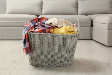 Photo of Wicker basket with dirty laundry on floor in living room