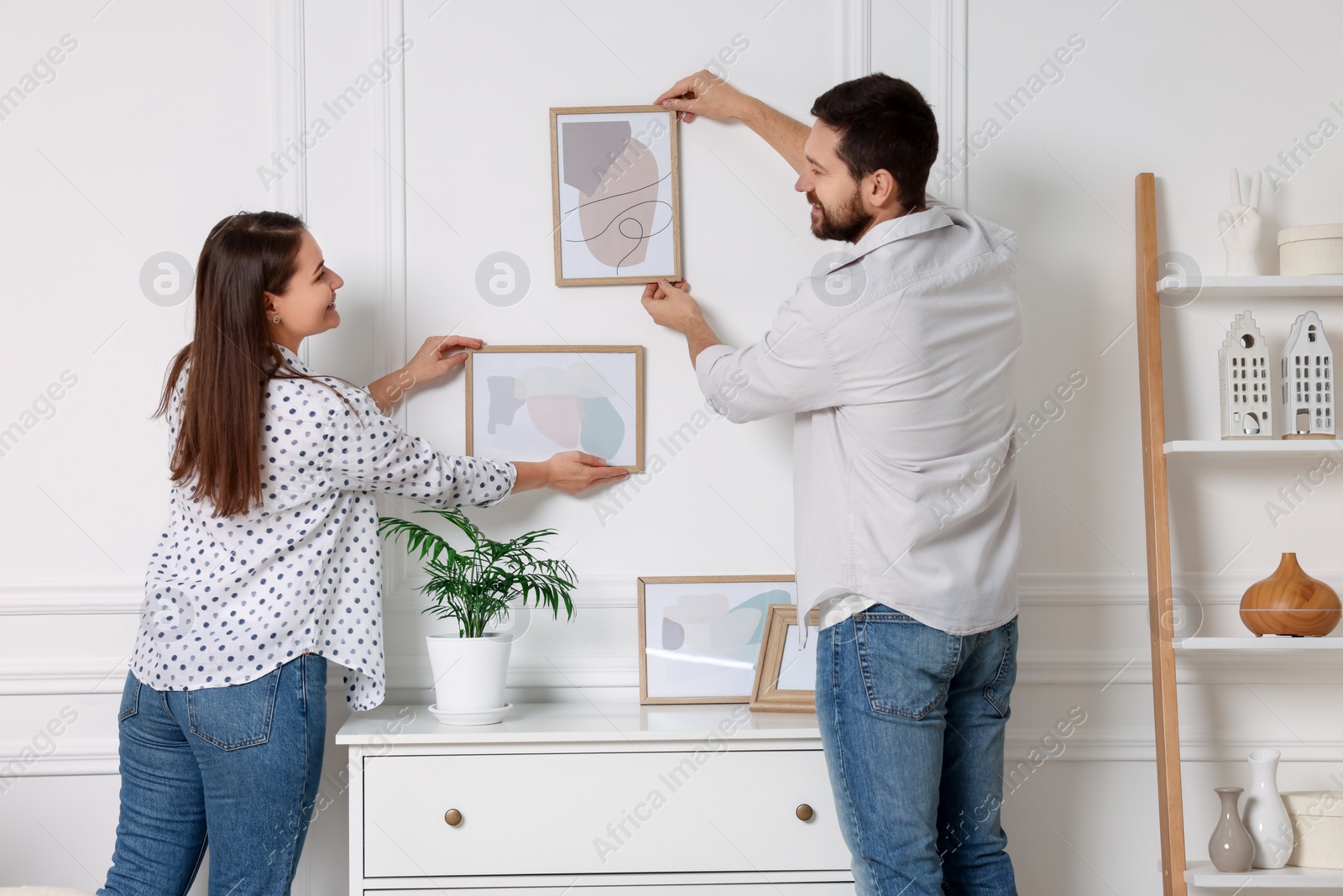 Photo of Man and woman hanging picture frames on white wall at home