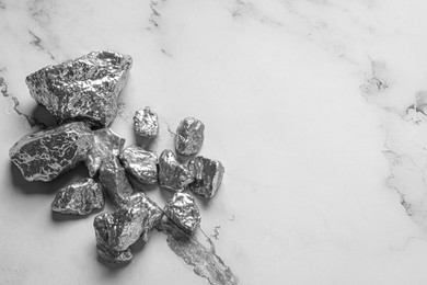 Pile of silver nuggets on white marble table, flat lay. Space for text