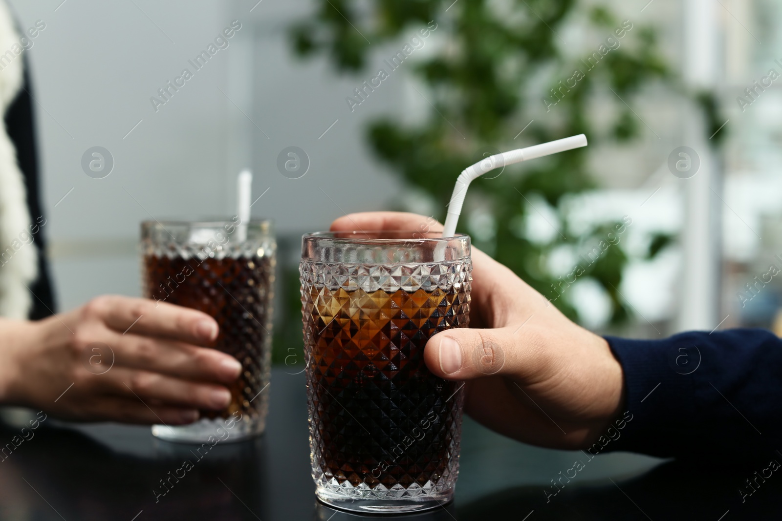 Photo of Couple with glasses of cold cola at table in cafe, closeup