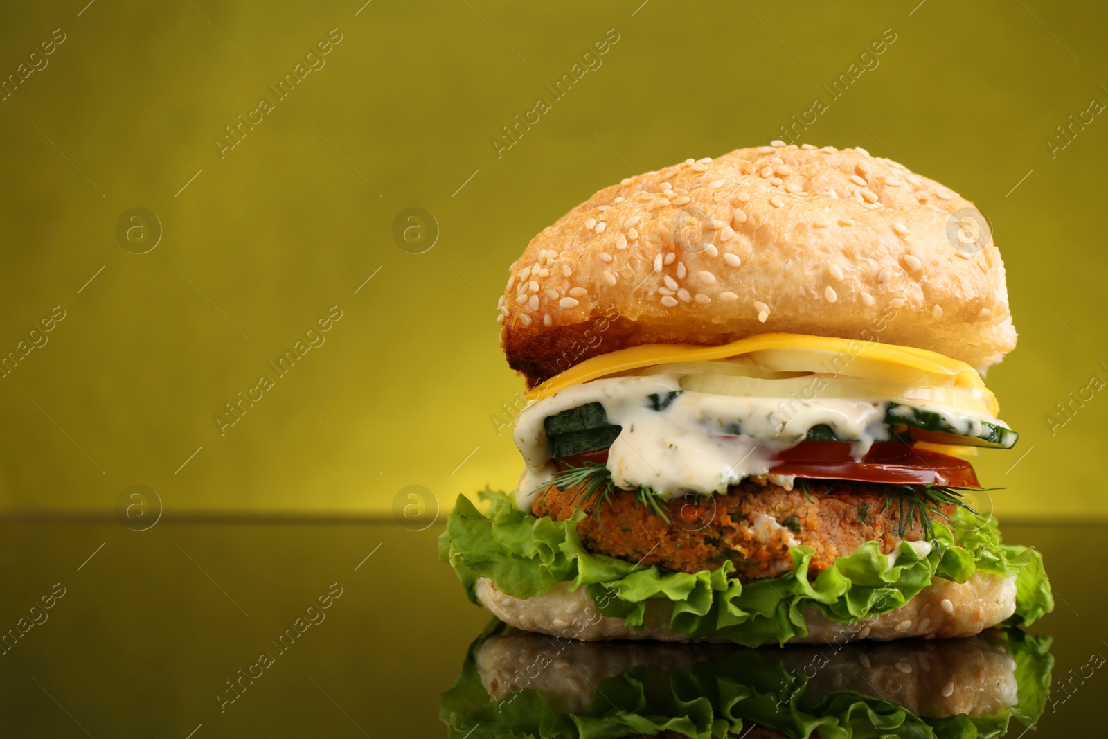 Photo of Delicious vegetarian burger on mirror surface against olive background, space for text