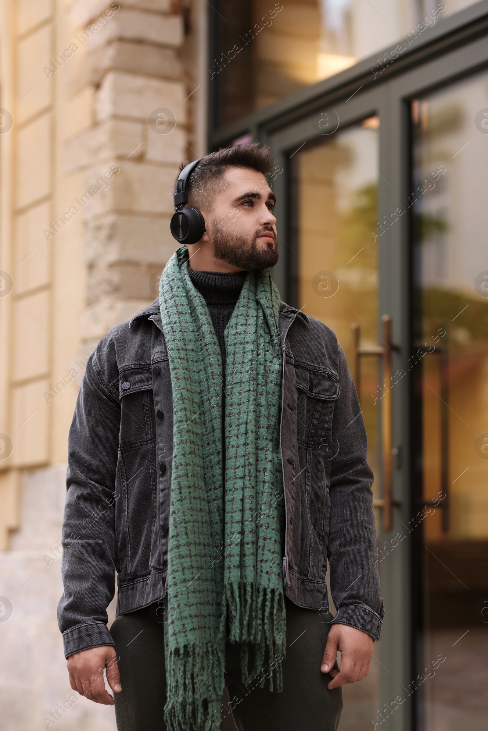 Photo of Handsome man in warm scarf and headphones on city street