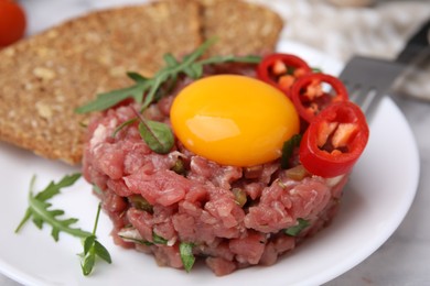 Photo of Tasty beef steak tartare served with yolk, pepper, bread and greens on white table, closeup