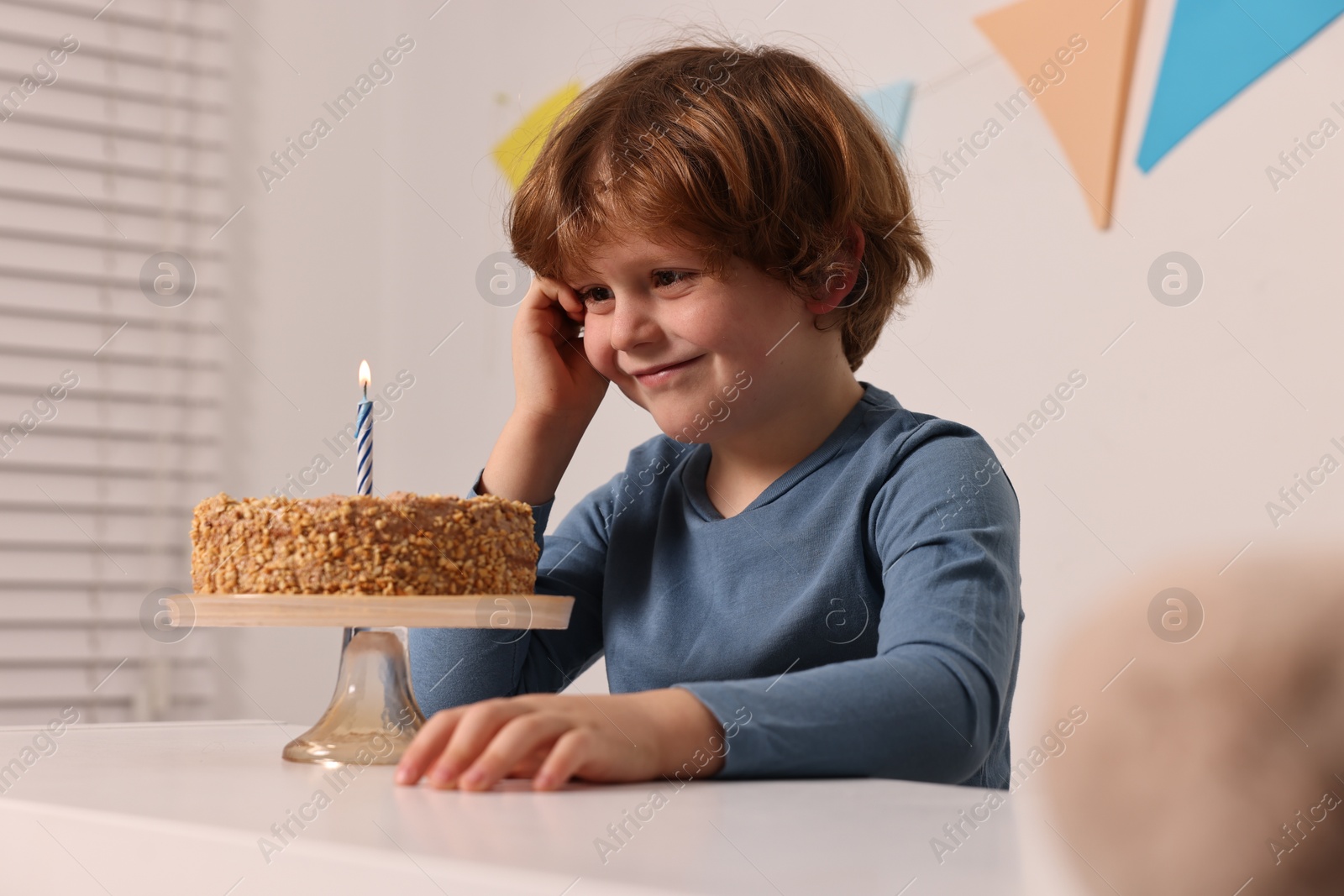 Photo of Cute boy with birthday cake at white table indoors