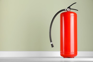 Photo of Fire extinguisher near pale green wall, space for text