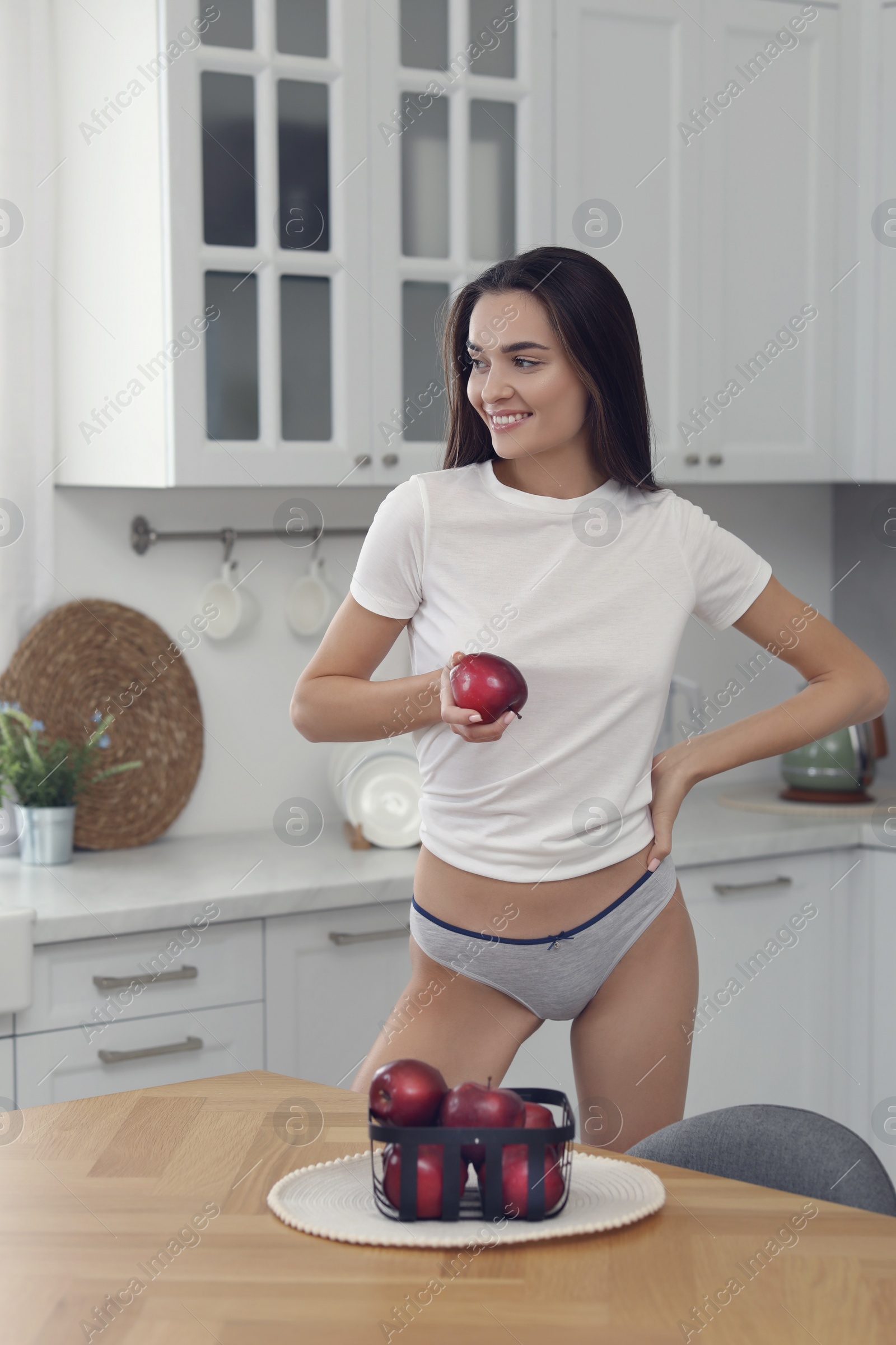 Photo of Young woman with apple in white t-shirt and comfortable underwear indoors