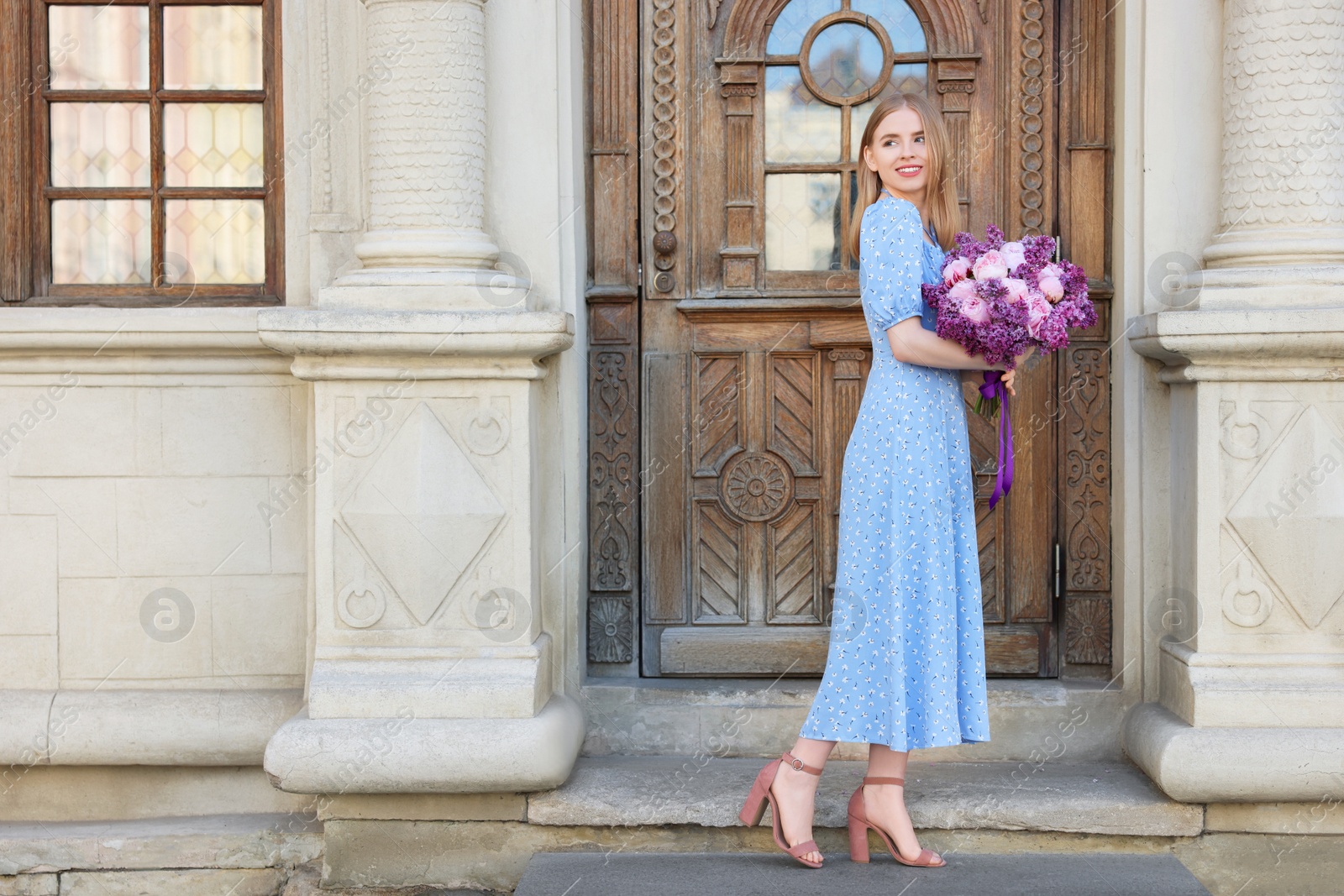 Photo of Beautiful woman with bouquet of spring flowers near building outdoors, space for text