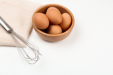 Raw eggs and whisk on white table. Baking pie