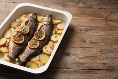 Baking tray with delicious roasted sea bass fish and potatoes on wooden table. Space for text