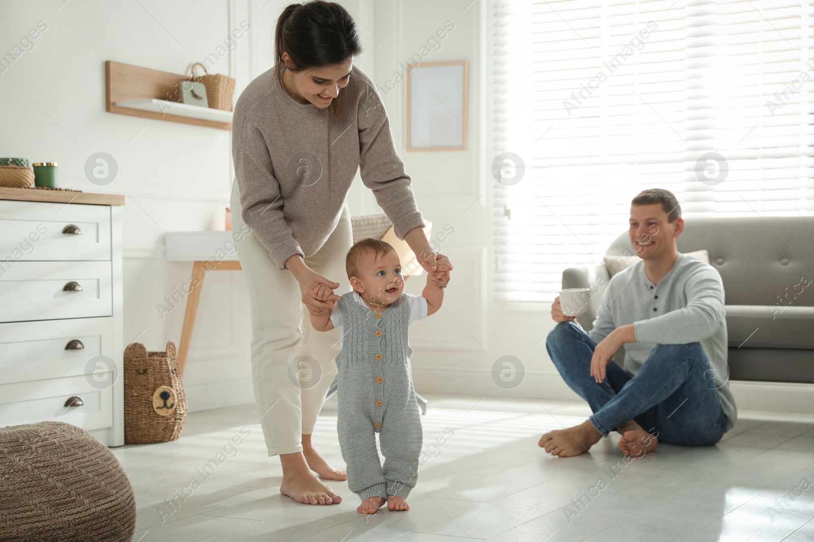 Photo of Mother supporting her baby daughter while she learning to walk at home