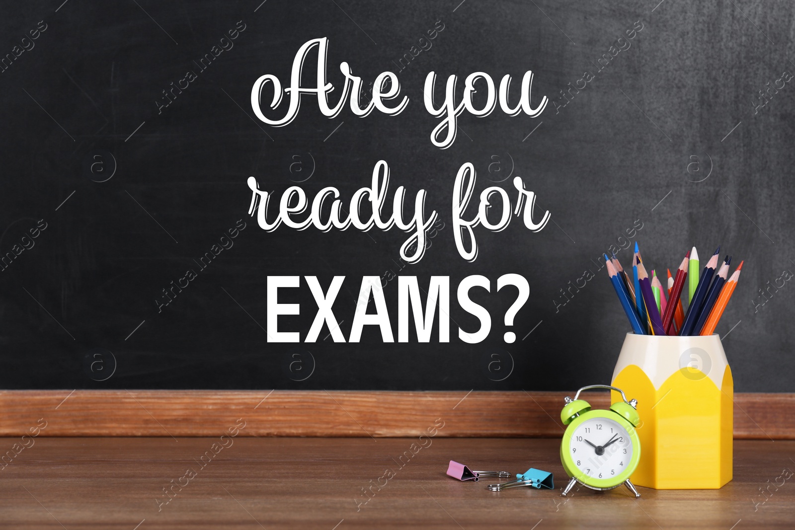 Image of Pencils and alarm clock on wooden table near blackboard with phrase ARE YOU READY FOR EXAMS