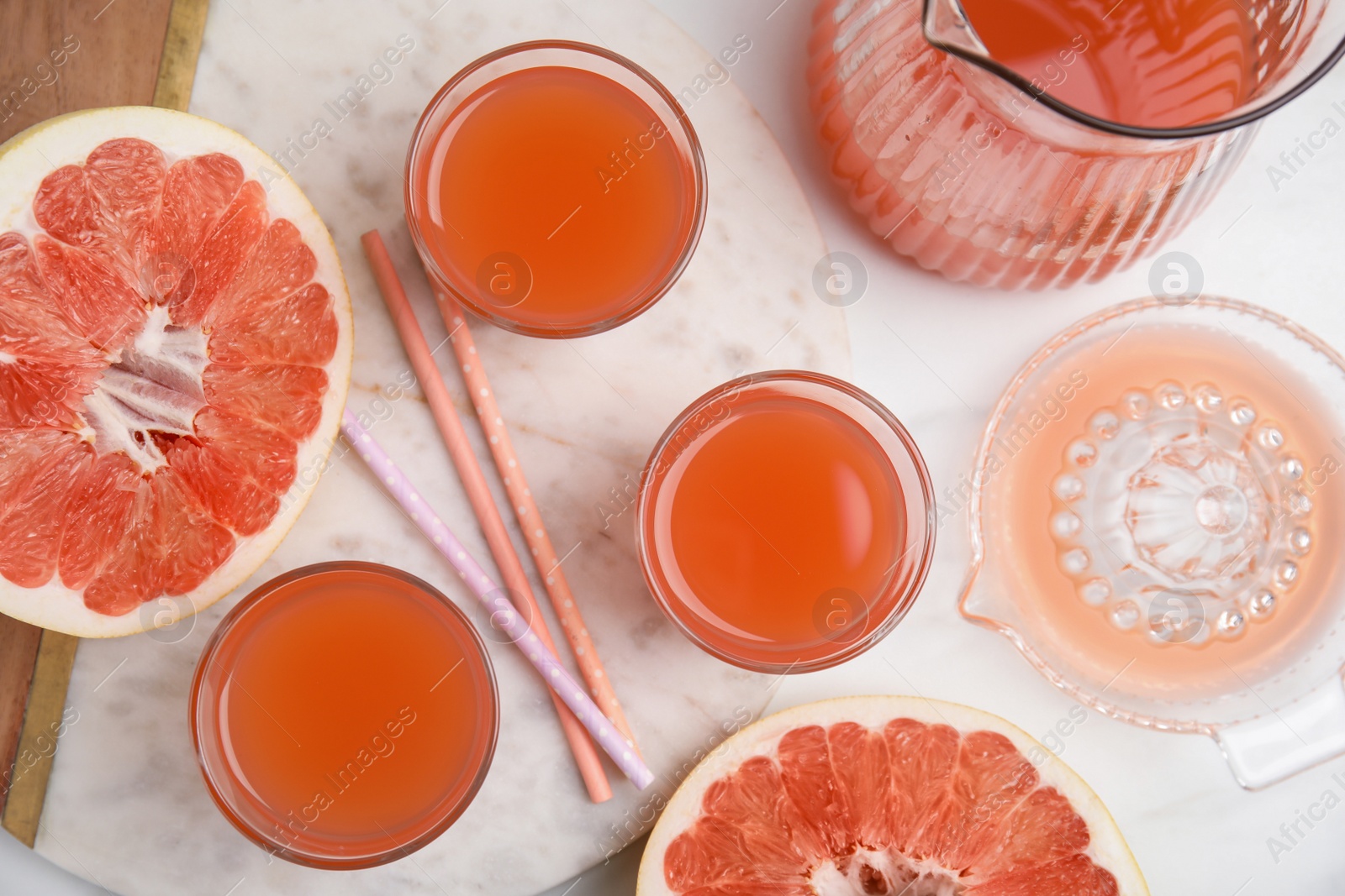 Photo of Glasses of pink pomelo juice with straws and fruit on white table, flat lay