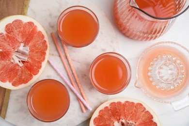 Photo of Glasses of pink pomelo juice with straws and fruit on white table, flat lay