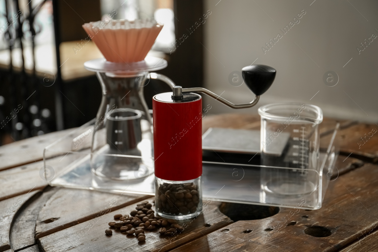 Photo of Manual coffee grinder with beans, glass jug and wave dripper on wooden table in cafe