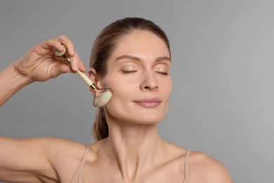 Photo of Woman massaging her face with jade roller on grey background