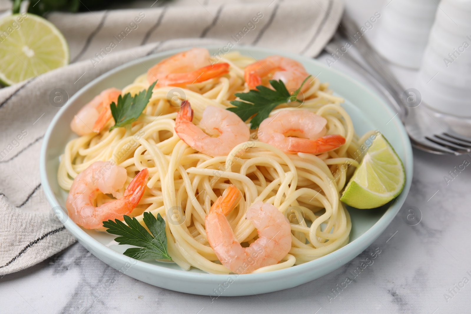 Photo of Tasty spaghetti with shrimps, lime and parsley on white marble table, closeup