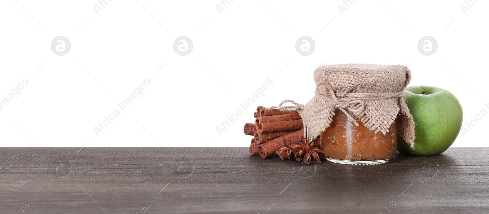 Photo of Jar with delicious apple jam, fresh fruit and cinnamon on wooden table against white background