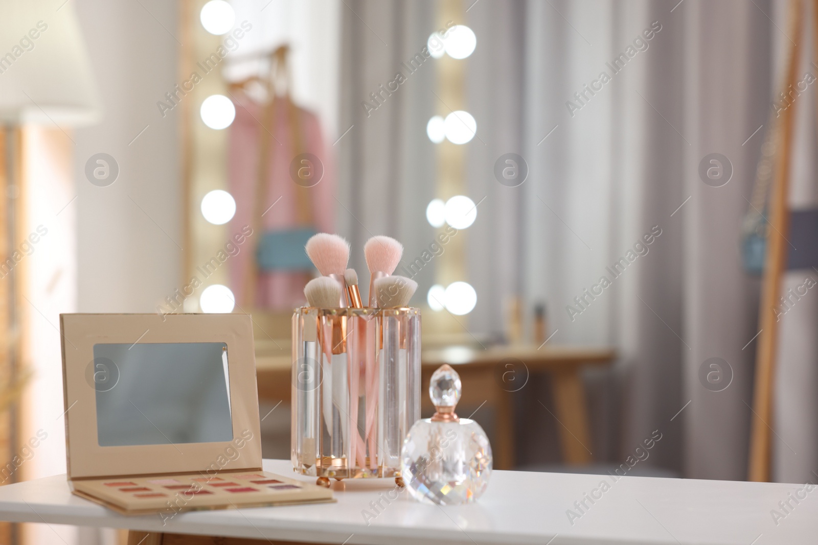 Photo of Set of brushes, eyeshadow palette and perfume on white table in makeup room, space for text