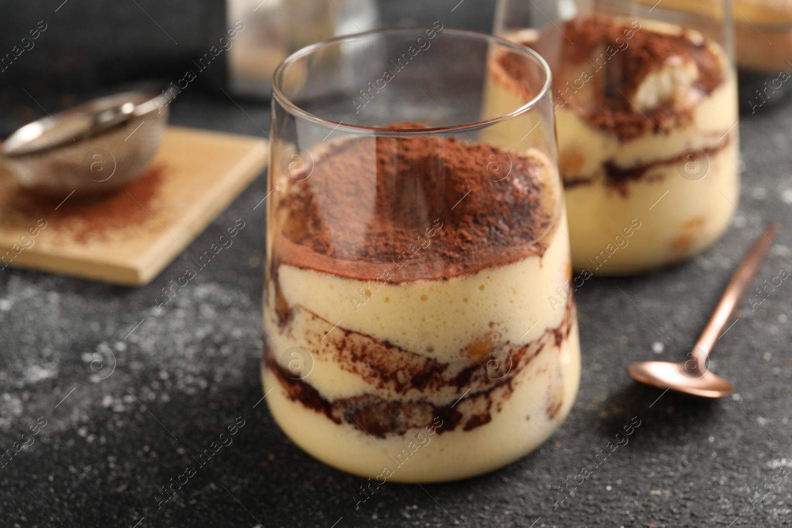 Photo of Delicious tiramisu in glasses on grey textured table, closeup