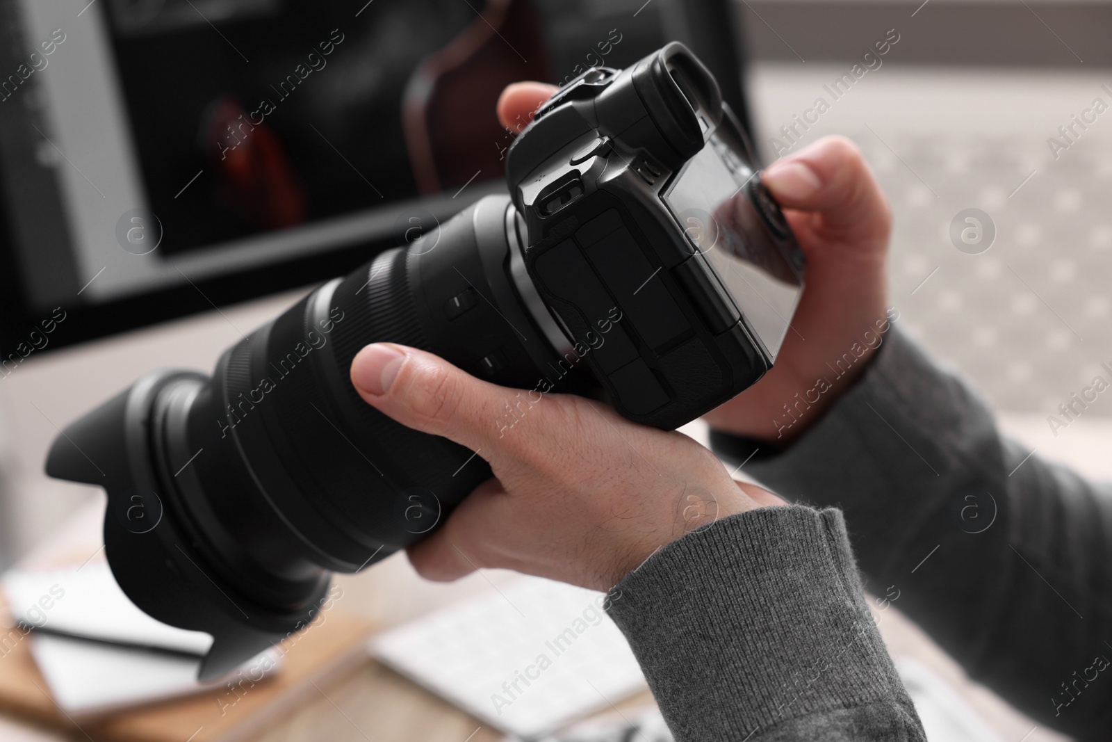 Photo of Professional photographer with digital camera at table indoors, closeup