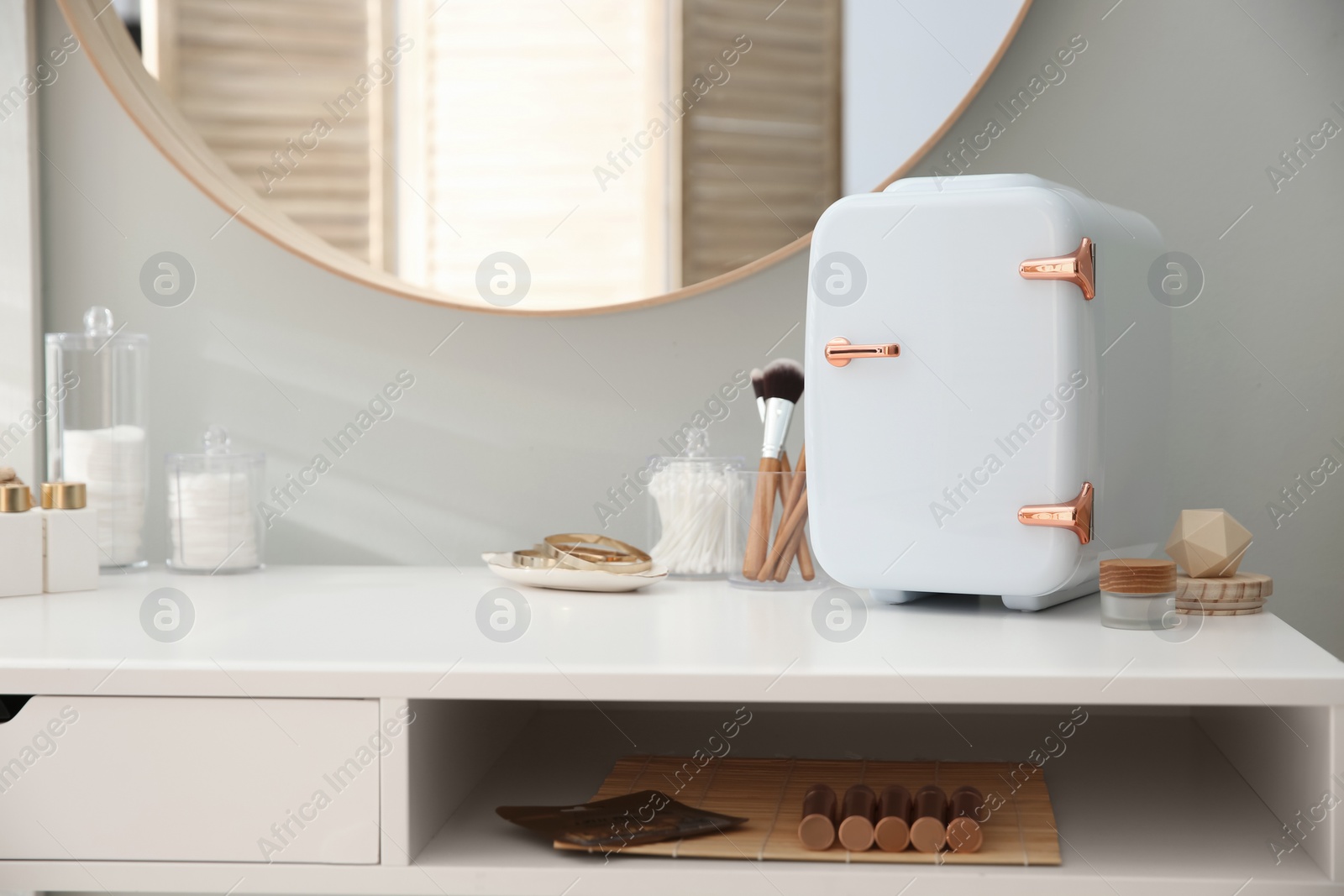 Photo of Cosmetics refrigerator and skin care products on white vanity table indoors