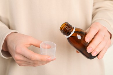 Photo of Woman pouring syrup from bottle into measuring cup, closeup. Cold medicine