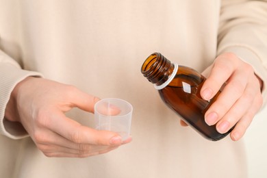 Woman pouring syrup from bottle into measuring cup, closeup. Cold medicine