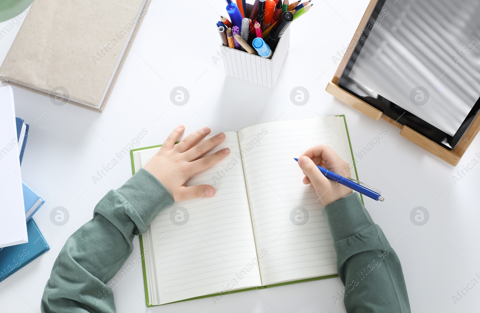 Photo of Cute little boy with modern tablet studying online at table, top view. E-learning