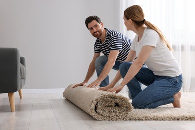 Photo of Smiling couple unrolling carpet on floor in room