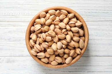 Photo of Organic pistachio nuts in bowl on wooden table, top view