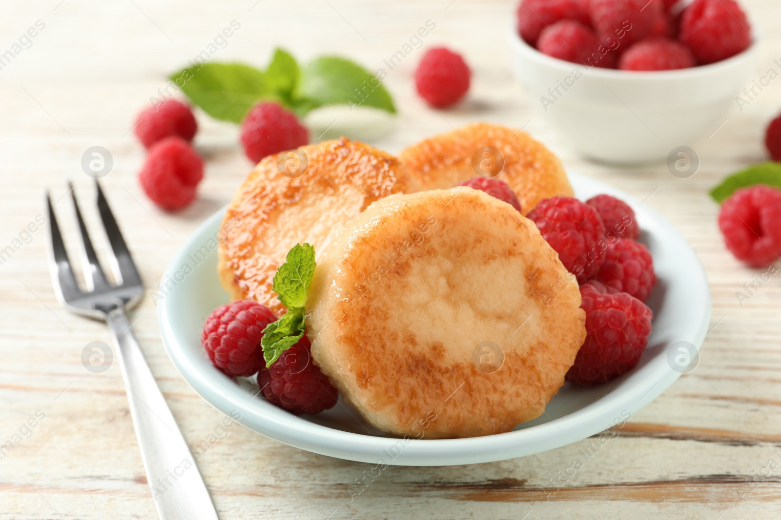 Photo of Delicious cottage cheese pancakes with raspberries and mint on white wooden table, closeup