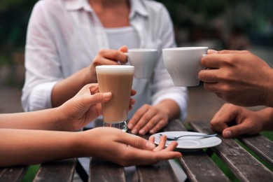 Friends drinking coffee at wooden table in outdoor cafe, closeup